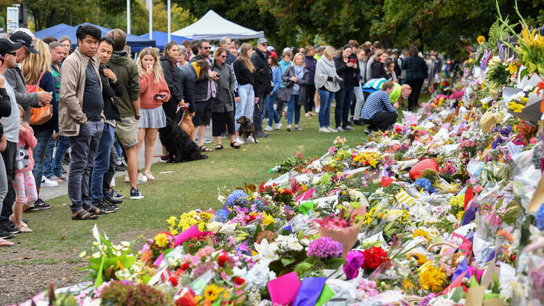 Trauernde Menschen legen Blumen an einen Zaun in den Botanischen Gärten in Christchurch.