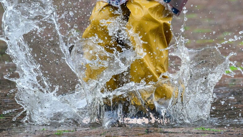 Ein Kind springt in Dresden in einer  sogenannten Matschhose und mit Gummistiefeln in eine Pfütze. Andere Wochenend-Aktivitäten fallen hingegen ins Wasser - viele Veranstaltungen wurden abgesagt.