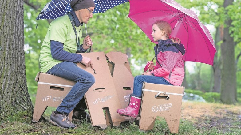 Felicia probiert einen Wellpappe-Campinghocker aus. Miterfinder Sven Gille von der TU Dresden zeigt der Achtjährigen, wie sie ihren Sitz zusammenfalten kann.