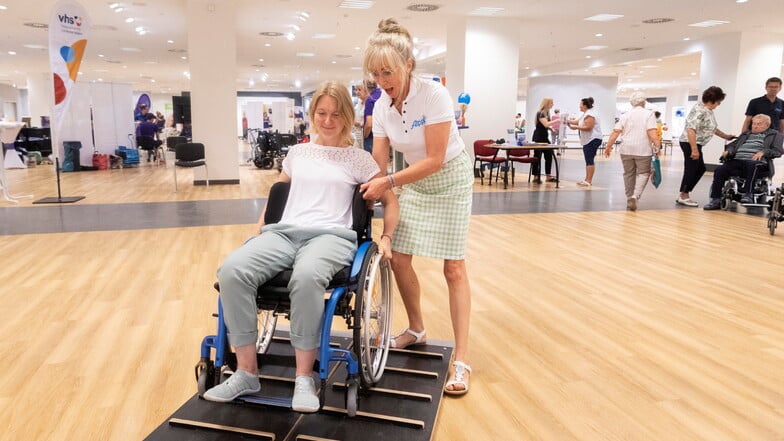 Annett Wagner (l.) testet, wie es ist, sich in einem Rollstuhl fortzubewegen. Katrin Neider vom Sanitätshaus Alippi unterstützt dabei.