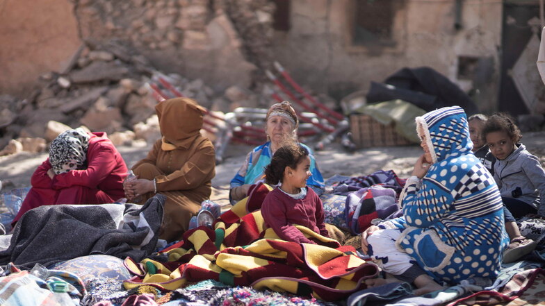 Familien sitzen vor ihren zerstörten Häusern.