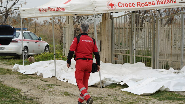 Ein Freiwilliger des italienischen Roten Kreuzes geht an einem Strand an den abgedeckten Leichen der Opfer eines gekenterten Bootes vorbei.