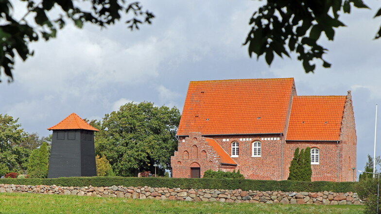 Die Kirche in Holeby mit romanischem Altarraum, gotischer Vorhalle und einem Glockenturm, der daneben steht.