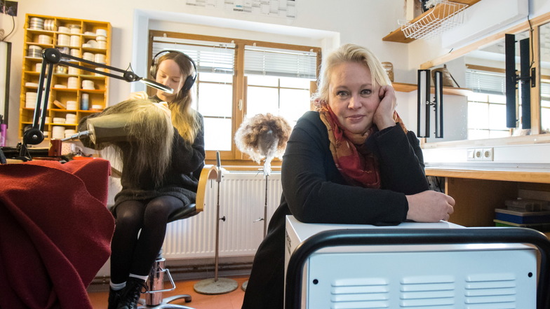 Sängerin Yvonne Reich stützt sich im November 2023 auf ein Trocknungsgerät in einer Werkstatt hinter der Bühne des Görlitzer Theaters. Im Hintergrund arbeitet Maskenbildnerin Catharina Nachtigal an einer Perücke.