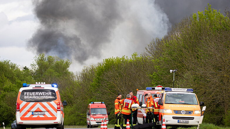 Einsatzkräfte der Feuerwehr stehen bei einem Großbrand in einem Braunschweiger Industriegebiet an ihren Einsatzfahrzeugen zusammen.