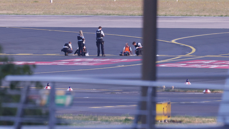 Polizisten stehen auf dem Flugfeld in Düsseldorf und versuchen Aktivisten der Gruppe "Letzte Generation" am Flughafen vom Asphalt zu lösen.