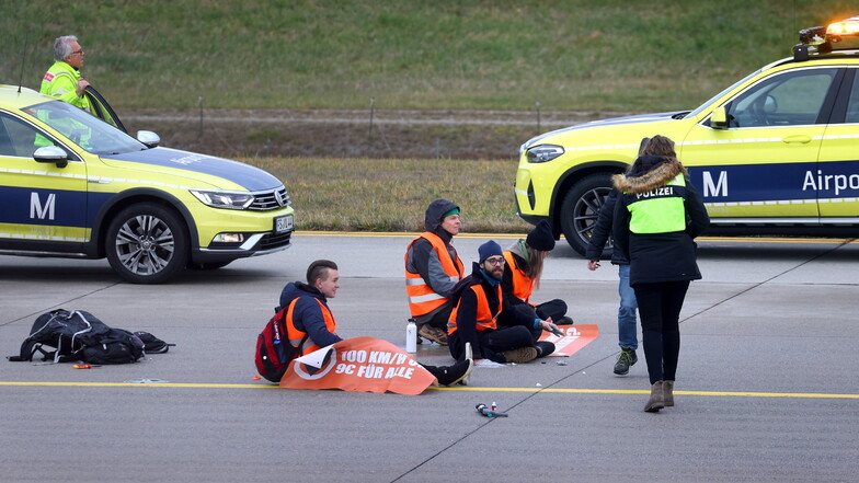 Vier Klima-Protestler sitzen mit angeklebten Händen auf dem Zubringer einer Start-und Landebahn am Airport Franz-Josef-Strauß.