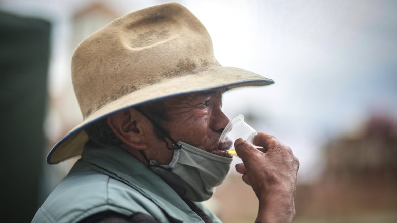 Ein Mann trinkt ein Gläschen Kamillentee, nachdem er durch eine Dampfkabine zur Vorbeugung von Atemwegserkrankungen gegangen ist. Die Kabine wurde in Bolivien vom Ministerium für Traditionelle Medizin aufgestellt.