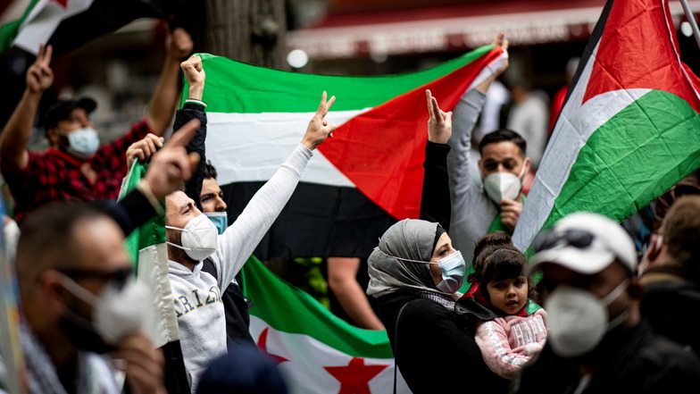 Teilnehmer der Demonstration verschiedener palästinensischer Gruppen laufen mit Palästina-Flaggen durch Neukölln.