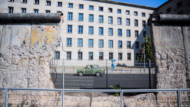 Ein Trabant fährt hinter einem Loch in einem Stück der verbliebenen Berliner Mauer vor dem Bundesfinanzministerium. Die Behörde will ein neues Amt in Dresden ansiedeln.
