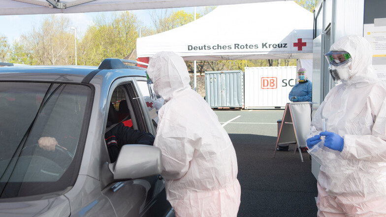 Mitarbeiter sind in Schutzanzügen im Dresdner Corona Test-Drive-in und testen im Auto.