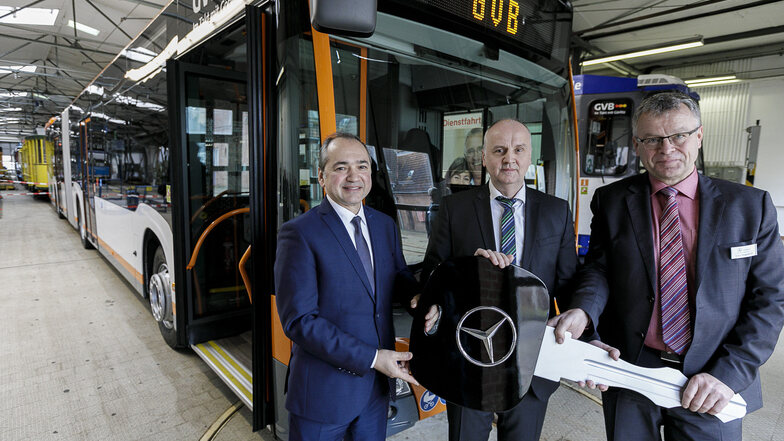Uwe Mauerhoff (r.), Vertriebsbeauftragter bei Mercedes-Benz Omnibusse, übergibt einen symbolischen Schlüssel für den neuen Hybridbus (im Hintergrund) an  Oberbürgermeister Octavian Ursu (l.) und GVB-Geschäftsführer Andreas Trillmich.