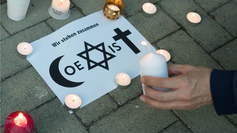 Ein Mann entzündet eine Kerze neben einem Schild mit der symbollastigen Aufschrift "Coexist"