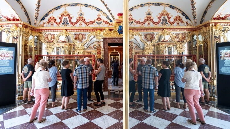 Besucher stehen im Historischen Grünen Gewölbe im Residenzschloss vor einer Vitrine mit den zurückerlangten Juwelen und spiegeln sich in einer Scheibe.