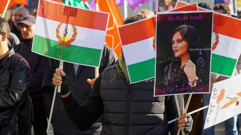 Auf einer Hamburger Demonstration tragen Iranerinnen und Iraner Flaggen und Bilder der jungen Mahsa Amini, die von iranischen "Revolutionswächtern" zu Tode geprügelt worden war, offenbar weil unter dem Hijab ihr Haar hervorschaute.