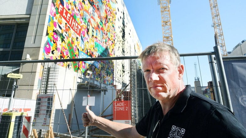 Der Leipziger Künstler Michael Fischer-Art steht am Bauzaun vor seinem Wandbild "Das Bild Zur Deutschen Einheit - 20 Jahre Friedliche Revolution".