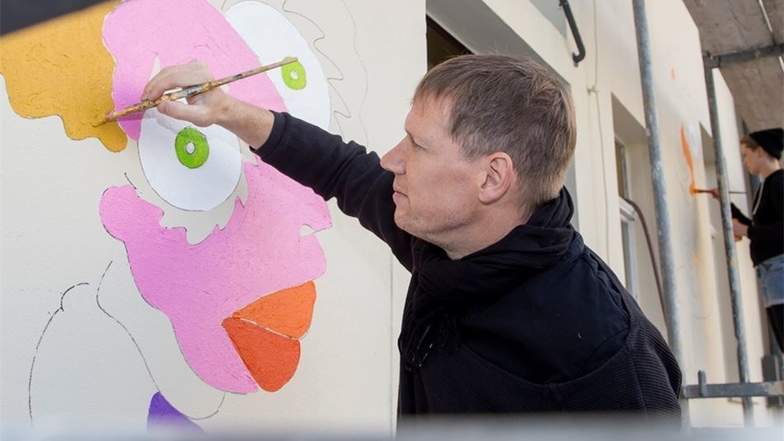 Er zeichnet vor, alle machen mit: Der Leipziger Künstler Michael Fischer-Art ist seit Donnerstag in Dorfhain, um die Fassade des Besucherzentrums aufzuhübschen. Dabei zeichnet er die Umrisse der Figuren vor. Einzelne Elemente werden dann verschiedenfarbig
