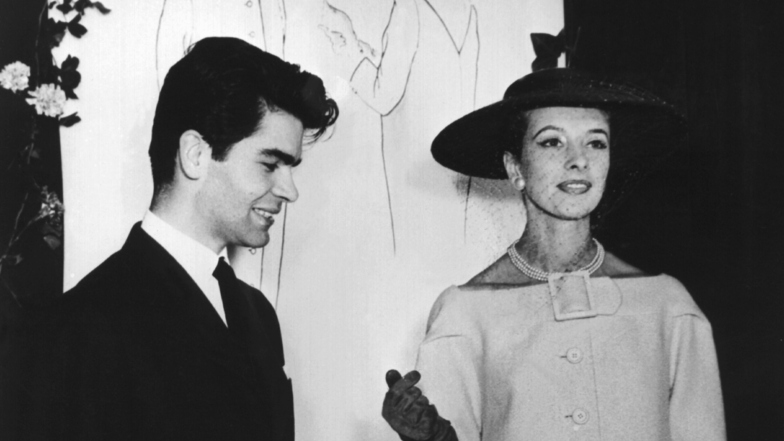 1953: Der erst 16-jährige (nach anderen Angaben 21-jährige) Hamburger Mode-Student Karl Lagerfeld 1954 mit einem Model beim Vorführen des Cocktail-Mantels. Foto: dpa