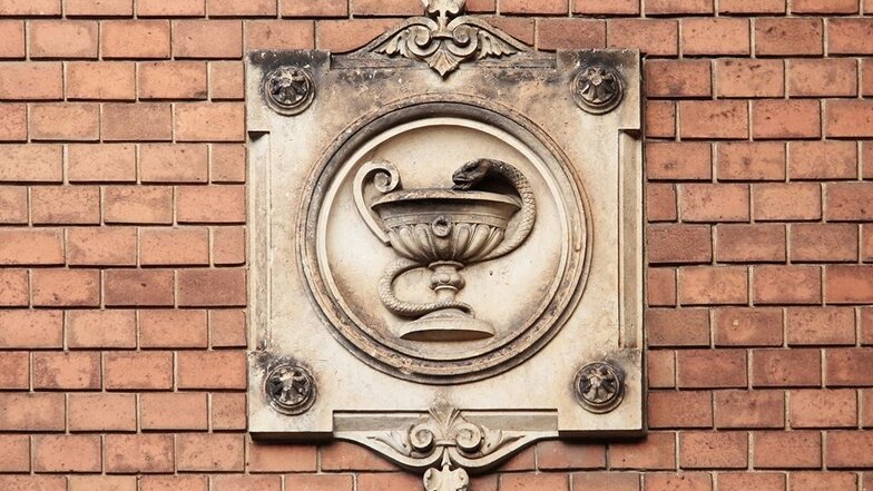 Symbolisch: Zeichen der Ärzteschaft ist eine Schlange, die sich um einen Stab ringelt. Dieser Fassadenschmuck dürfte eine Variation davon sein.