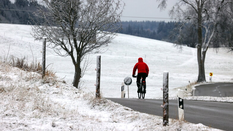Bayern, Friesenried: Ein Radfahrer fährt durch die mit Neuschnee bedeckte Landschaft.