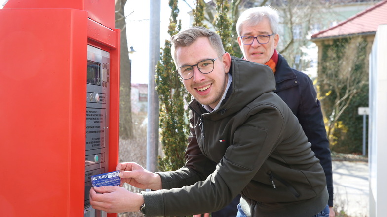 An Kamenzer Parkscheinautomaten weisen jetzt Aufkleber auf die Möglichkeit der Ticketbuchung per Smartphone hin. Christian Hartmann (vorn), Digitalisierungsbeauftragter der Stadt, und Ordnungsamtsleiter Joachim Hoyer haben sie angebracht.