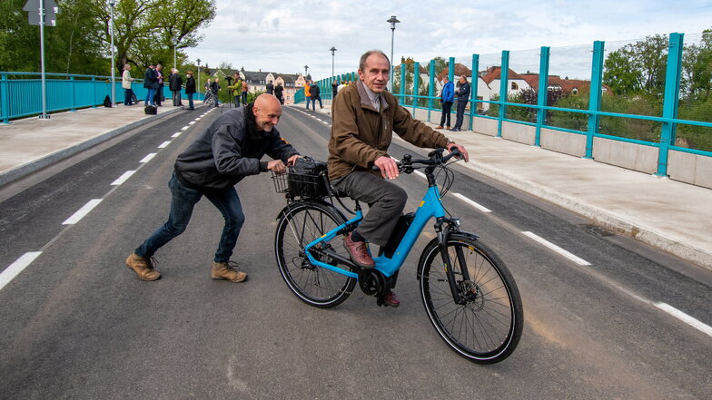 Lothar Seifert fährt mit seinem Rad als erster über die Brücke. Sven Weißflog, Chef der Firma Bau Logistik, schiebt ihn an.