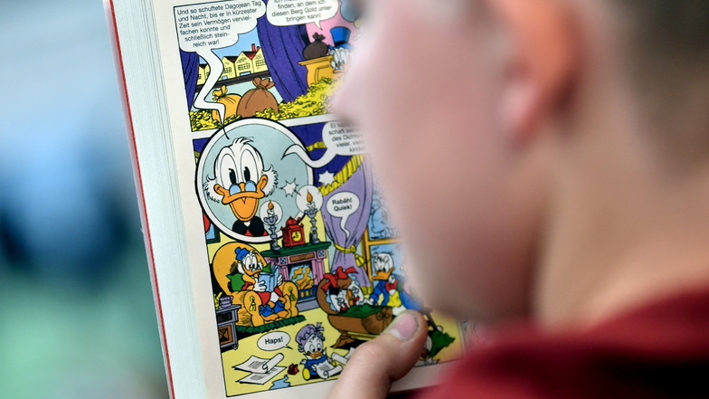 Ein Junge schaut sich eine Comic-Geschichte um Dagobert Duck in einem Taschenbuch an.