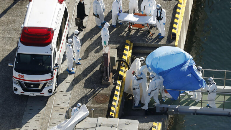 Medizinisches Personal in Schutzanzügen begleitet im Hafen von Yokohama einen Passagier, der positiv auf das Coronavirus getestet wurde. 