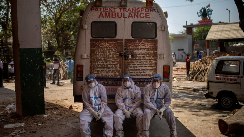 Indien, New Delhi: Erschöpftes medizinisches Personal, die Opfer, die an den Folgen einer Corona-Infektion verstorben sind, zur Einäscherung bringen, sitzen auf der hinteren Stufe eines Krankenwagens in einem Krematorium.