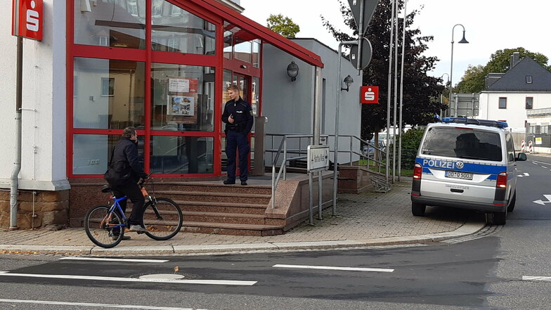 Ein Polizist steht nach dem Überfall vor dem Eingang zur Sparkasse in Hartha. Er weist eine Passantin darauf hin, dass die Filiale nicht betreten werden darf.