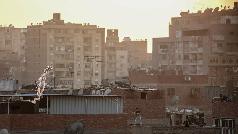 Ein Junge steht in Gizeh auf einem Dach und lässt einen handgefertigten Drachen über Wohnhäuser im Al-Munib-Viertel fliegen.