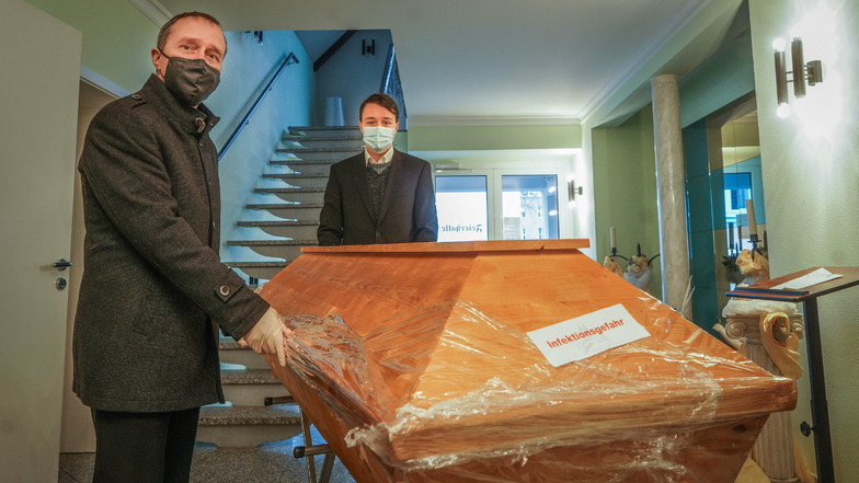 Dirk Jurschik (l.) vom Bestattungsunternehmen Schröter und sein Sohn Florian bereiten einen Sarg mit einem verstorbenen Covid-19-Patienten zur Überführung ins Krematorium nach Meißen vor.