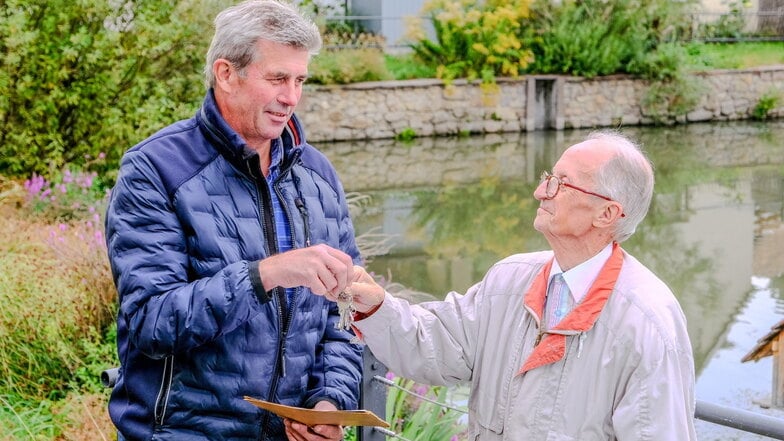 Am Dorfteich nimmt Uwe Forke (l.) von Siegfried Schneider den Schlüsselbund zu allen wichtigen Türen in Wahnsdorf entgegen. Darunter ist der für das Gemeindezentrum. Dort leitet Forke künftig die Beratungen des Ortschaftsrats.