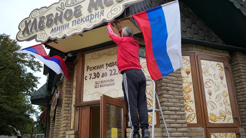 Ein Mann hängt russische Fahne an einem Café in Luhansk auf.