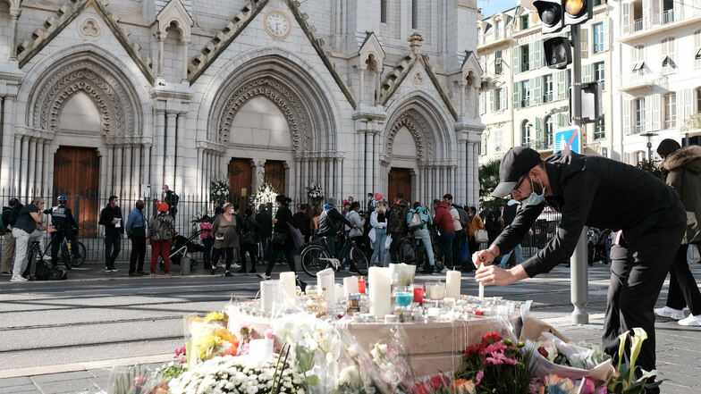 Frankreich, Nizza: Ein Mann zündet vor der Notre-Dame-Basilika zwischen Blumen eine Kerze an. Nach der brutalen Attacke wollen Anti-Terror-Ermittler herausfinden, ob der Tatverdächtige möglicherweise von Komplizen unterstützt wurde.
