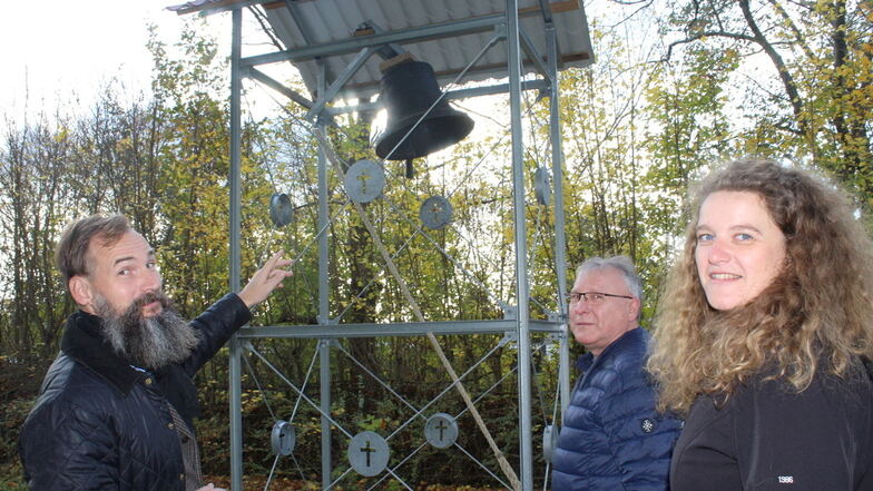 Pfarrer Martin Scheiter (links) zeigt auf den neuen Glockenturm auf dem Urnenfriedhof Nünchritz. Bürgermeisterin Andrea Beger (rechts) und ihr Vorgänger Gerd Barthold (Mitte) haben sich für ihn eingesetzt.