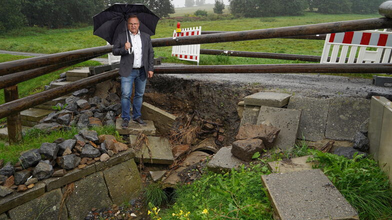 Die Brücke an der Weststraße in Neukirch, an der Bürgermeister Jens Zeiler auf diesem Foto einen Monat nach dem Hochwasser steht, wird noch nicht grundhaft saniert. Die Gemeinde wartet noch auf eine Fördermittelzusage.