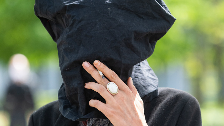 Dresden: Eine Teilnehmerin einer Kundgebung trägt einen Sack über den Kopf und raucht durch ein Loch eine Zigarette.