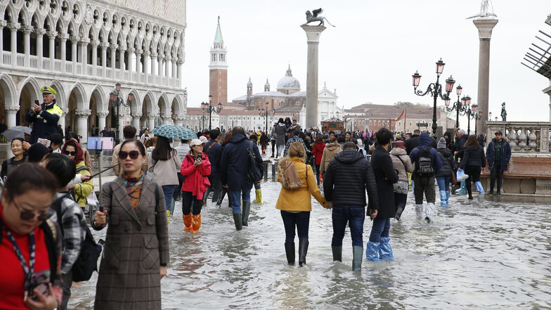 Touristen laufen auf dem überfluteten Markusplatz durch das Wasser. Fast das komplette historische Zentrum steht unter Wasser.