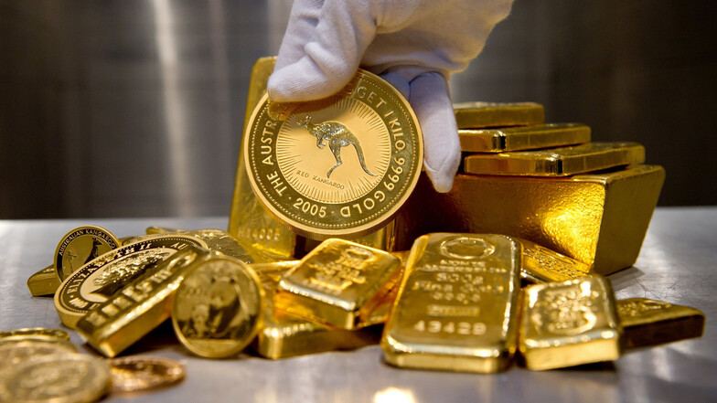 Eine Hand hält bei einem Goldhändler in München eine 1.000g-Goldmünze. Daneben liegen Münzen und Goldbarren in unterschiedlichen Größen.