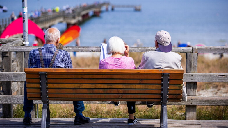 Drei Senioren sitzen auf einer Bank an der Ostsee.