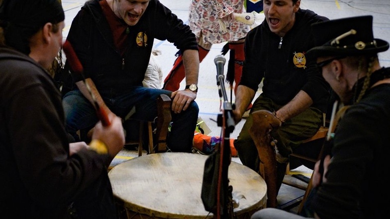 Die Musiker sitzen im Kreis und schlagen gemeinsam auf eine Trommel. Dazu erklingen indianische Gesänge.