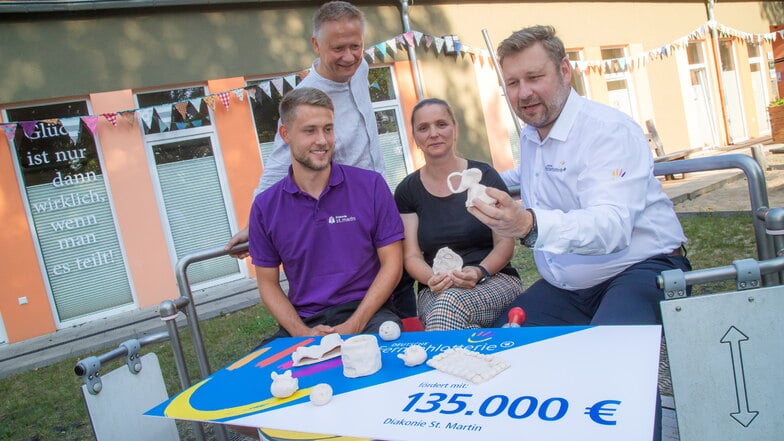 Stephan Masch (rechts) von der Deutschen Fernsehlotterie bei der Übergabe des Förderschecks an die Sozialarbeiter Luca Pluta und Ilka Schönberg. Im Hintergrund Diakon Stefan Zeller.