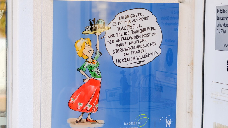 Das Hinweisschild hat der Grafiker Lutz Richter gestaltet. Die abgebildete Frau symbolisiert die Stadt Radebeul, zu erkennen unter anderem am Stadtwappen auf ihrem Kleid.