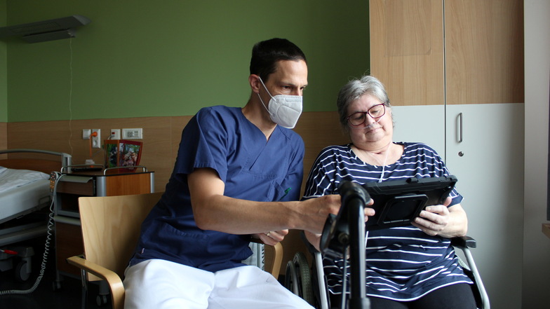 Ein Mitarbeiter hilft einer Patientin bei der technischen Bedienung des Gerätes.