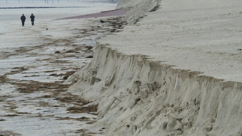 Besucher spazieren an der Abbruchkante des Strandes.