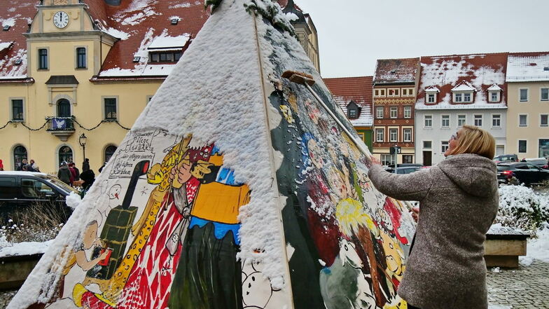 Geschützt gegen Witterung und Böller ist jetzt der Marktbrunnen in Lommatzsch. Bürgermeisterin Anita Maaß (FDP) kehrt den Schnee weg, damit die kunstvollen Malereien von Joachim Zehme zu sehen sind.