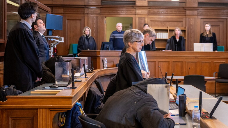 Vier Angeklagte sitzen vor Beginn der Verhandlung in Begleitung ihrer Anwälte im Gerichtssaal.
