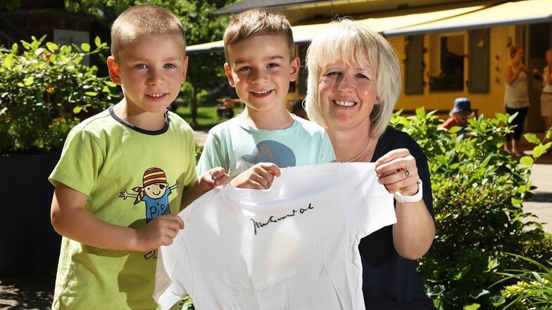 Die Kirschbergkinder Baldur (4), Emil (5) sowie Kita-Chefin Gabriela Mentzer zeigen das T-Shirt, auf dem Ali bei seinem Besuch 2002 in Riesa unterschrieben hat.