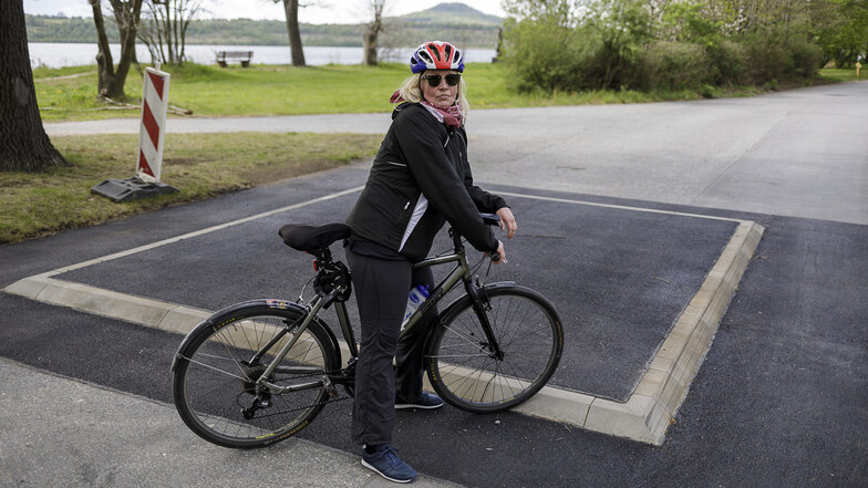 Stadträtin Yvonne Reich steht mit ihrem Fahrrad an einem der sechs neuen Huckel am Rundweg um den Berzdorfer See – hier in Deutsch Ossig.